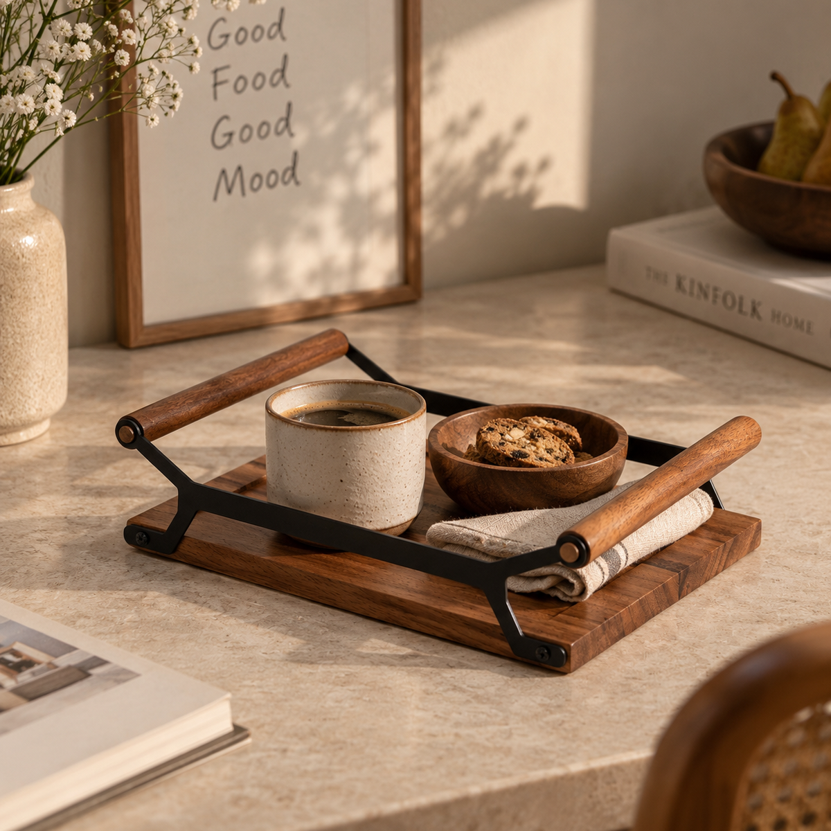 A wooden serving tray with black metal handles and legs, styled on a light stone countertop. The tray holds a ceramic mug of coffee, a small wooden bowl of cookies, and a folded cloth napkin.