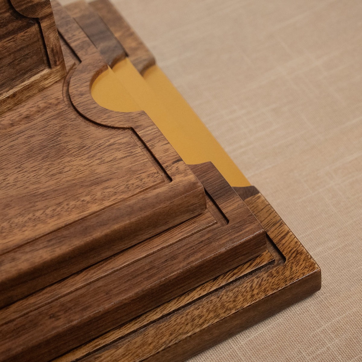 Close-up of a dark brown wooden tray or serving board with a gold-colored inner lining, resting on a beige textured fabric surface.