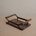 A rectangular wooden serving tray with a dark brown wood grain finish and black metal handles, shown on a neutral beige textured surface against a solid beige background.